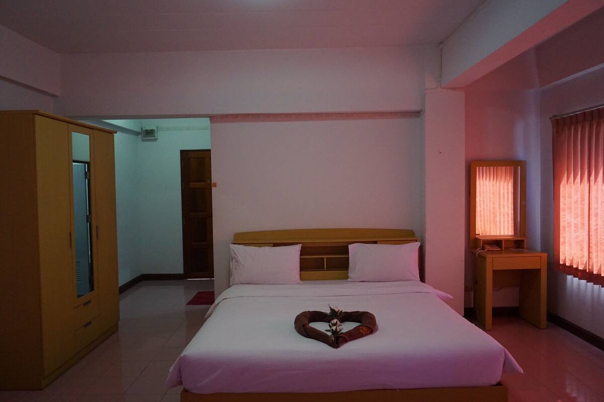 A hotel room with a bed, a wooden wardrobe, a desk with a lamp, and a window with curtains.