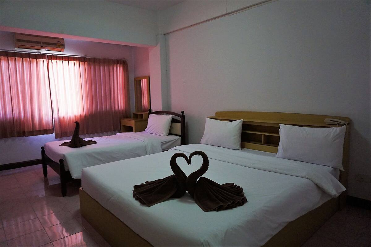 A hotel room with two beds, a window with curtains, an air conditioning unit, and a bedside table.