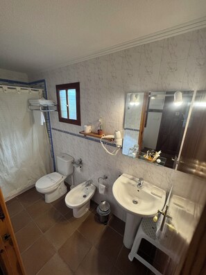 Un baño con inodoro, bidé y lavamanos, un espejo y una cortina de ducha.