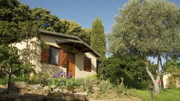A house with a stone foundation, wooden shutters, and a garden with various plants and a tree.
