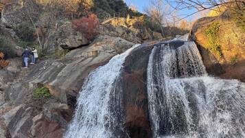 Una cascada que cae sobre rocas, con una persona de pie en un saliente cercano.