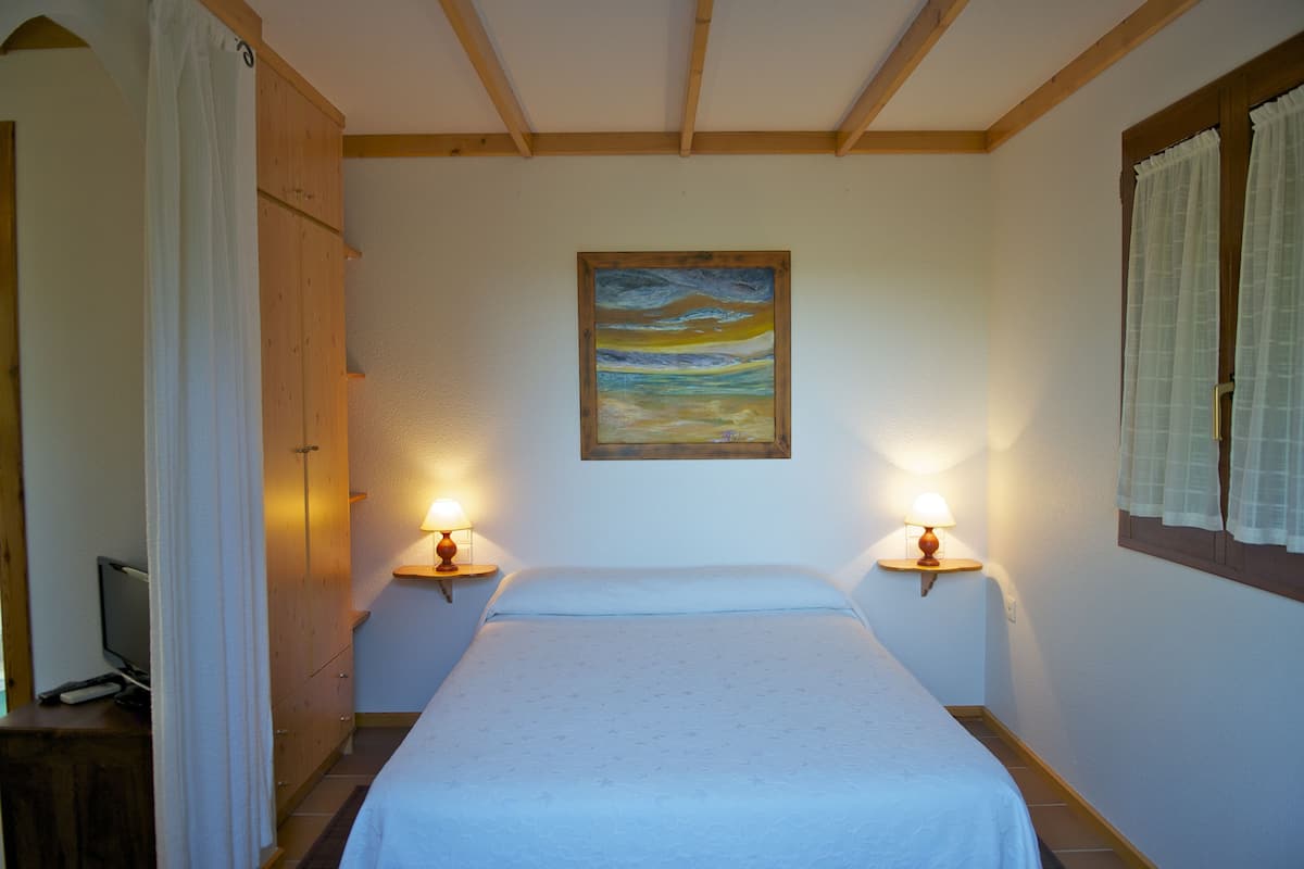 Et soveværelse med en seng, to sengeborde med lamper, et billede på væggen og en træskab.
