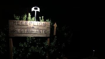 Un letrero de madera con la inscripción 'RECEPTION RESTAURANTE' y una flecha que apunta hacia arriba, rodeado de follaje y rocas.