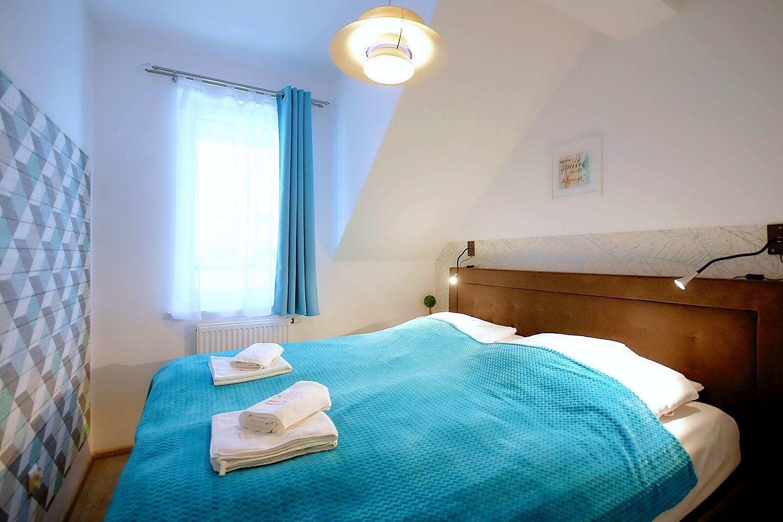 Un dormitorio con cama, ventana con cortinas, cabecero con luz y pared con diseño geométrico.