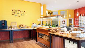 A breakfast buffet area with a coffee machine, fruit, bread, and various condiments.
