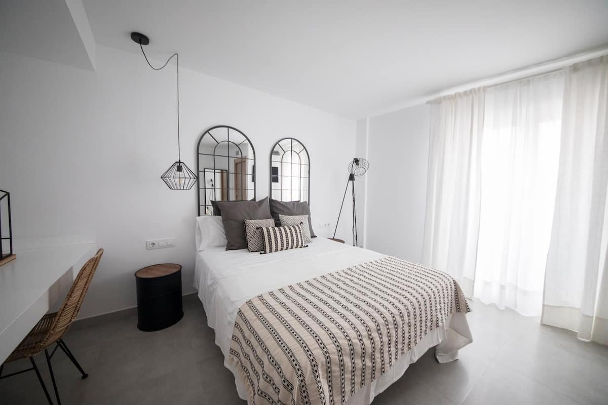 Un dormitorio moderno con una cama grande, dos lámparas de noche, un cesto redondo y una silla de mimbre.