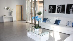 Un moderno hall de hotel con una mesa de centro de vidrio, sofás blancos y almohadones con estampado azul y blanco.
