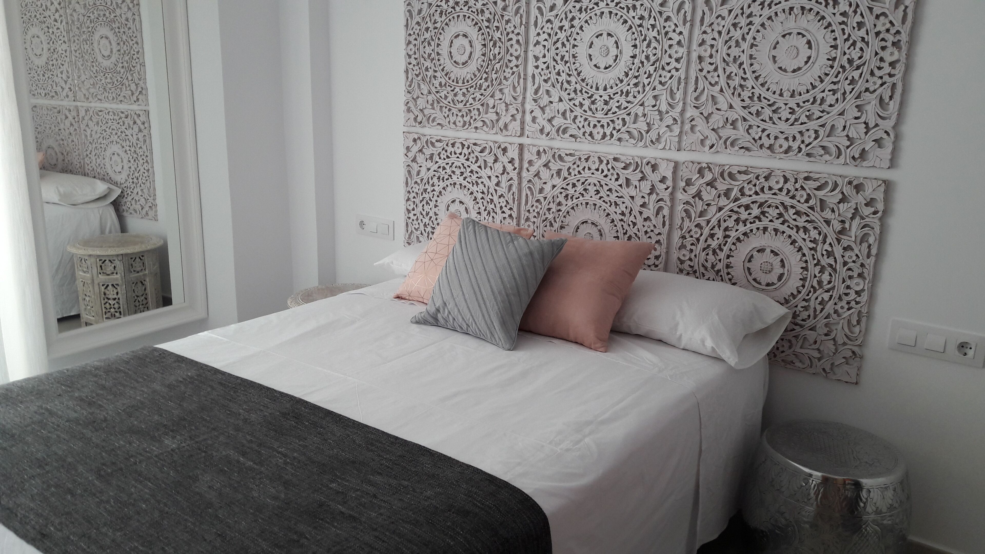 A neatly made bed with a grey and pink pillow, a grey throw blanket, and a decorative wall panel with intricate patterns.
