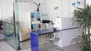 Un área de recepción con un mostrador de vidrio, un sofá blanco y una unidad de estanterías azul con ficheros.