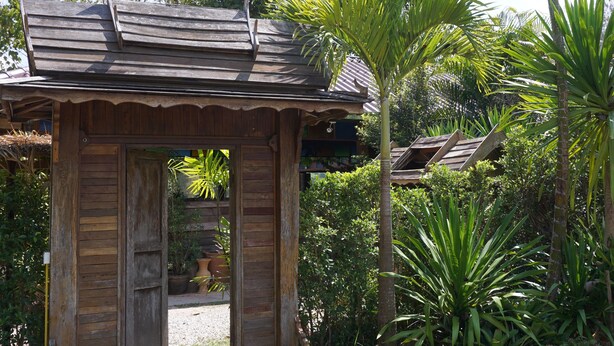A rustic wooden structure with a sloped roof, surrounded by lush greenery and palm trees. - Phuruarounmai Resort (Phu Ruea)
