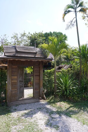 A rustic wooden structure with a sloped roof, surrounded by lush greenery and palm trees. - Phuruarounmai Resort (Phu Ruea)