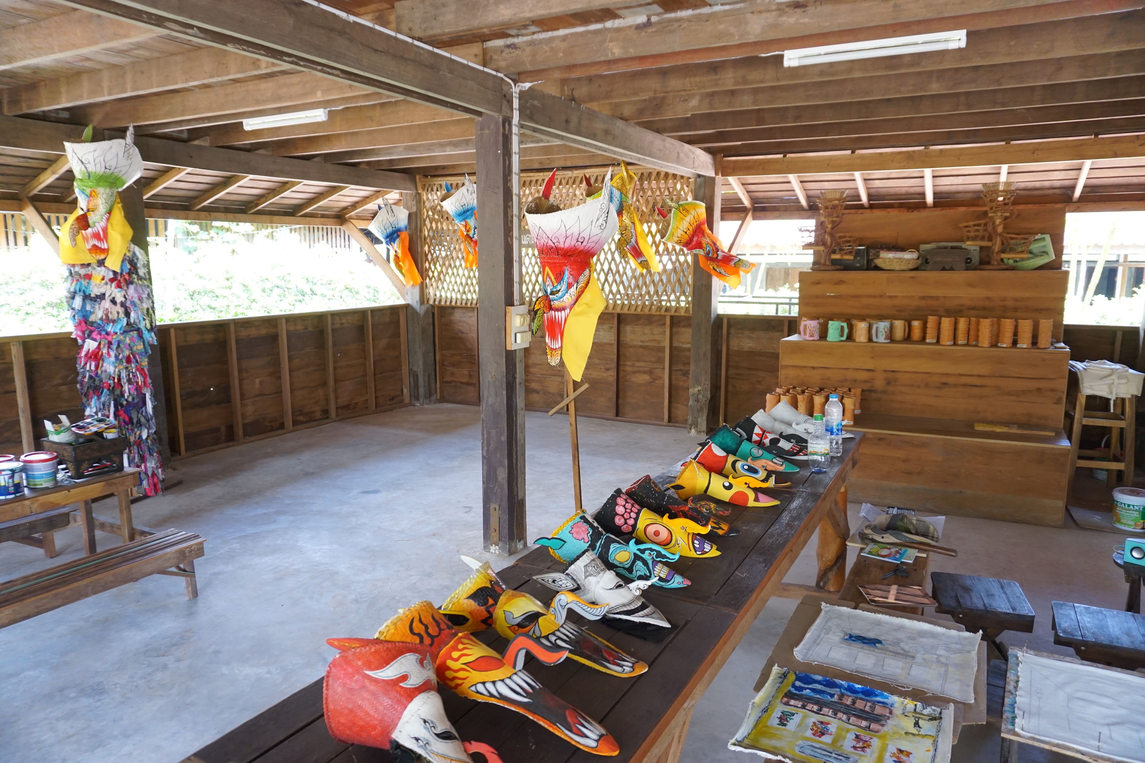 A room with a long table displaying various colorful masks and a wooden bench.