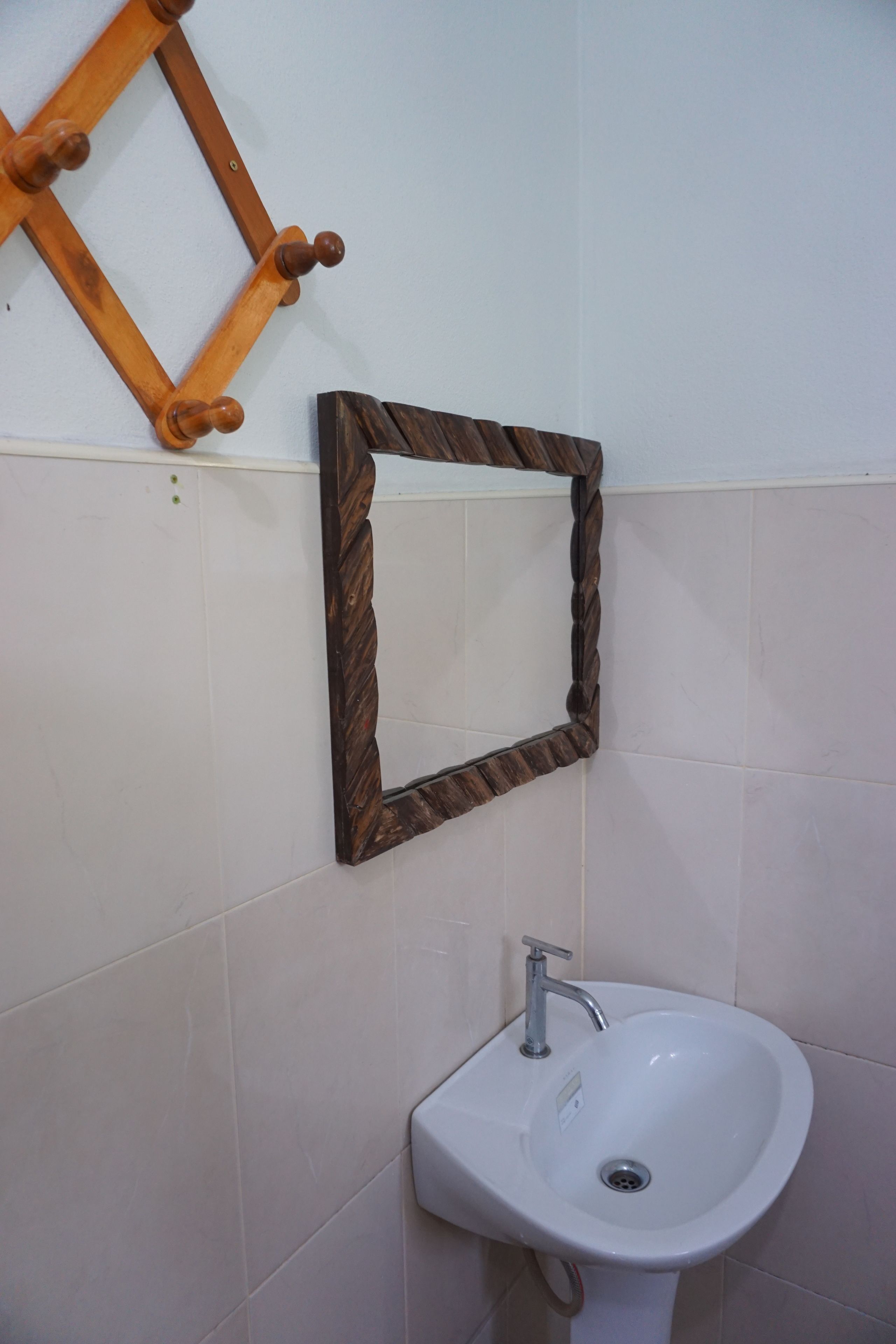 Un baño con un lavamanos blanco, un perchero de madera y un espejo con marco retorcido.