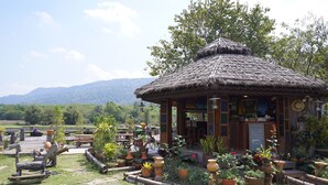 A rustic hut with a thatched roof surrounded by potted plants and outdoor seating. - Phuruarounmai Resort (Phu Ruea)