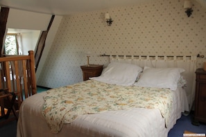 A bedroom with a bed, a nightstand, a lamp, and a wooden chair.