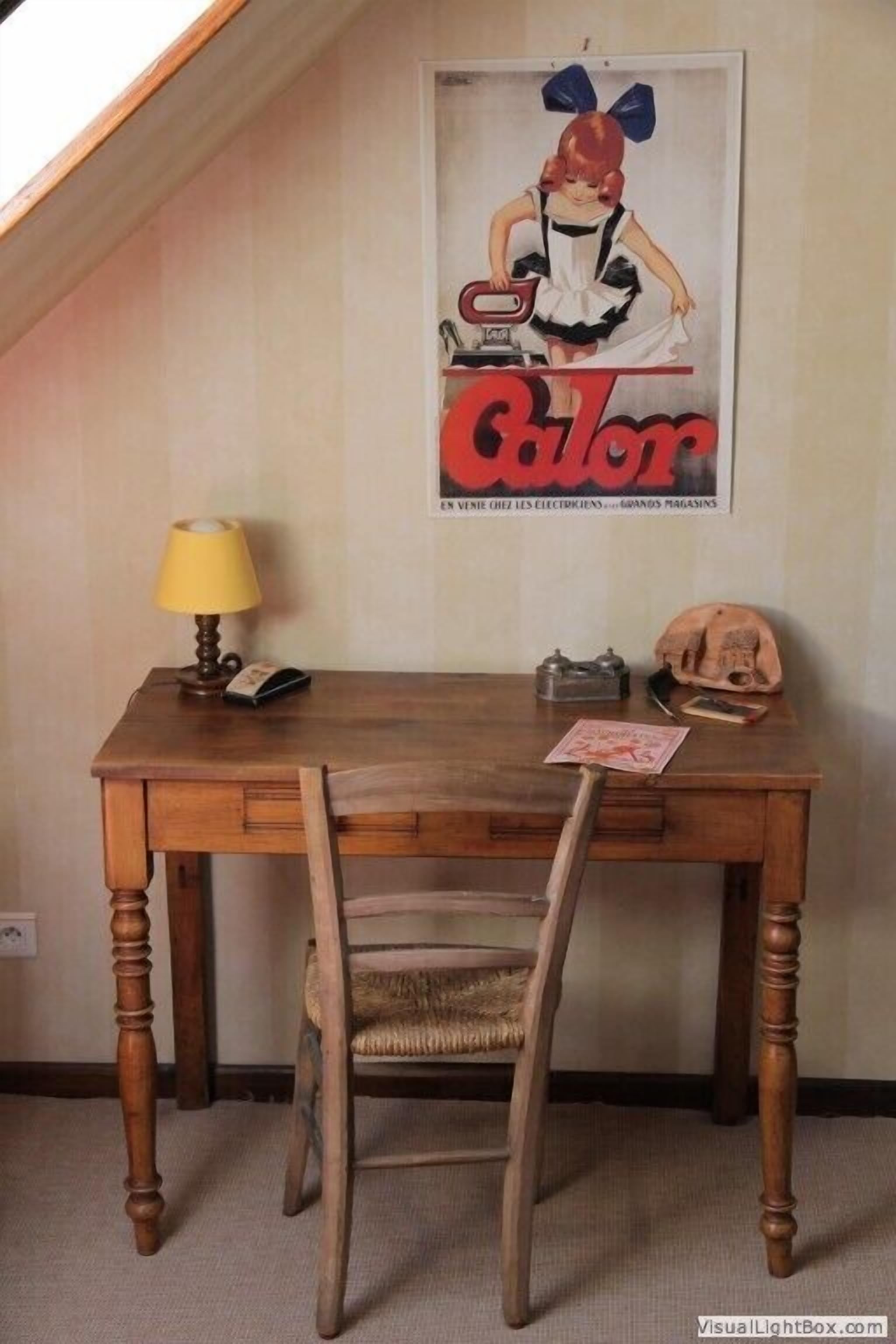 A wooden desk with a lamp, a vintage poster, and a skull on the wall.