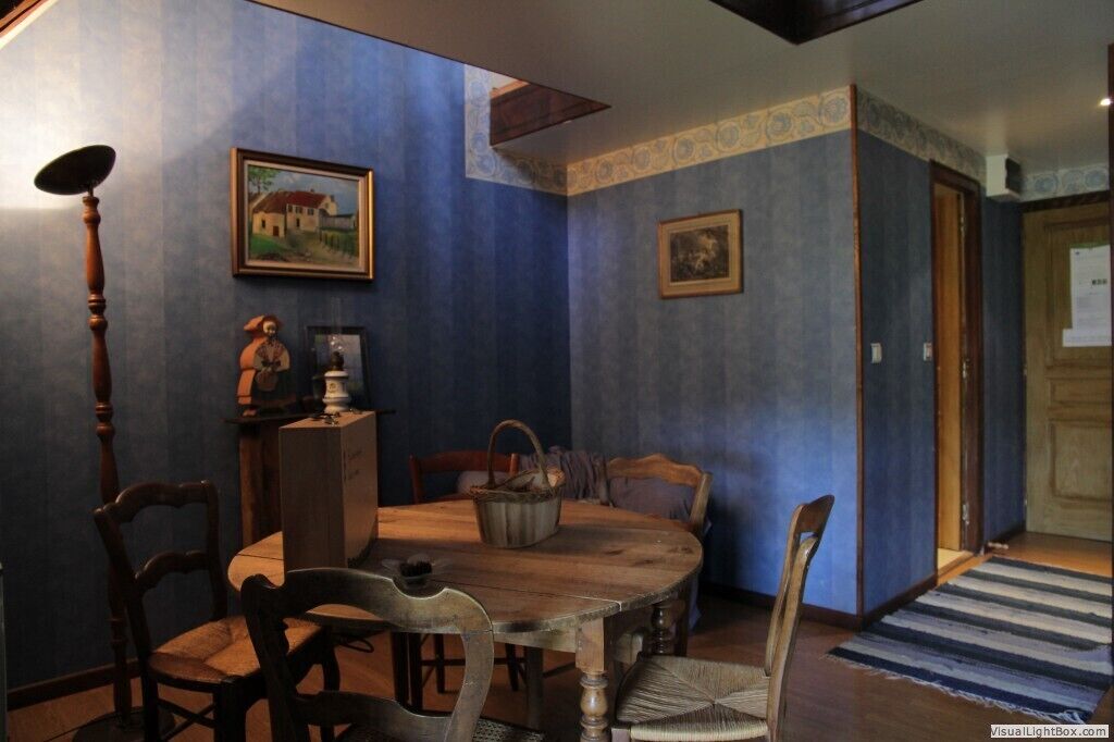 Un comedor con una mesa y sillas de madera, una pared azul con un detalle decorativo y un cuadro sobre la mesa.