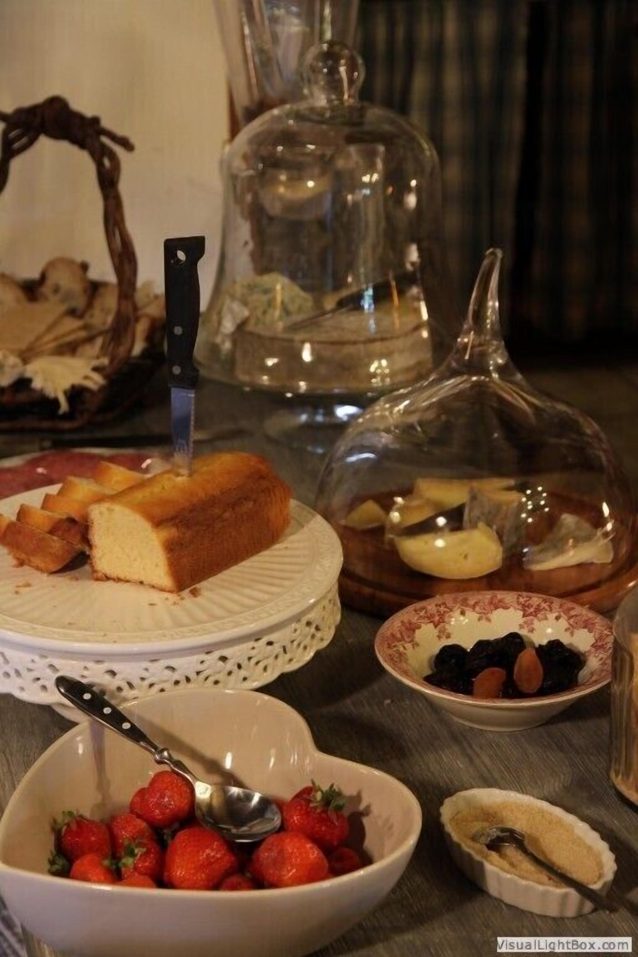 A table with a cake, a bowl of strawberries, and a covered dish with various items.