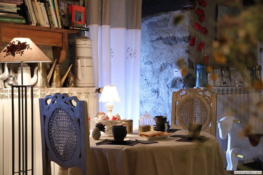 Un comedor acogedor con una mesa dispuesta para dos personas, que incluye una lámpara, un hervidor de té y objetos decorativos.