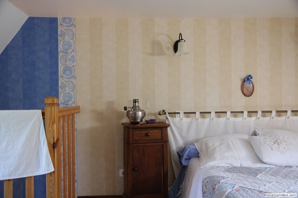 A bedroom with a bed, a nightstand, a wall-mounted lamp, and a wooden chair.