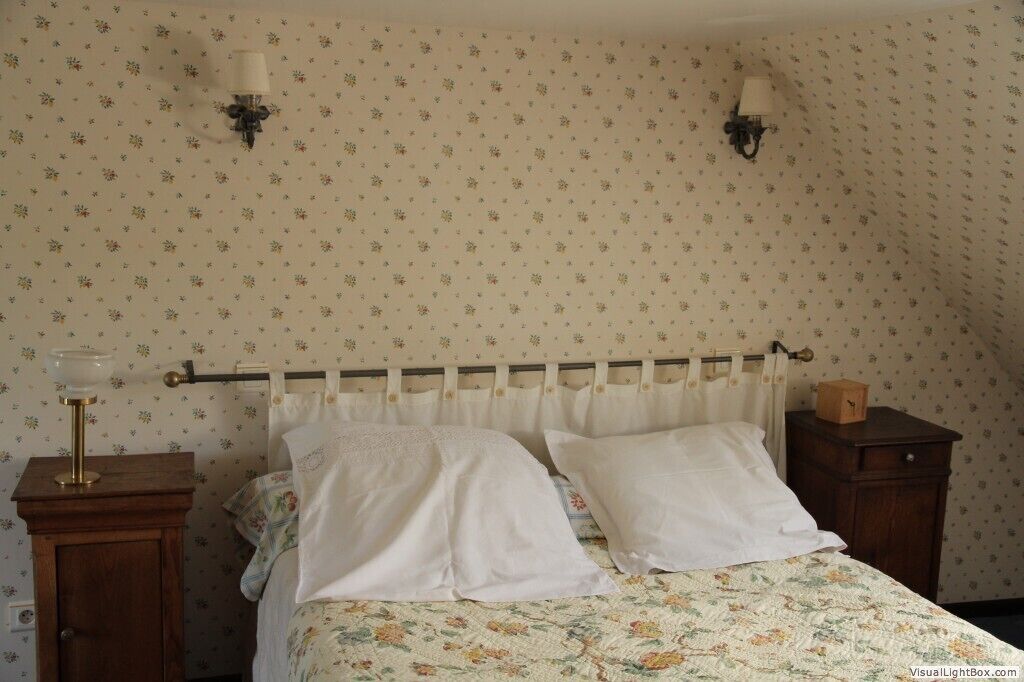 Un dormitorio con una cama, dos lámparas de pared, una mesita de noche y un armario de madera.