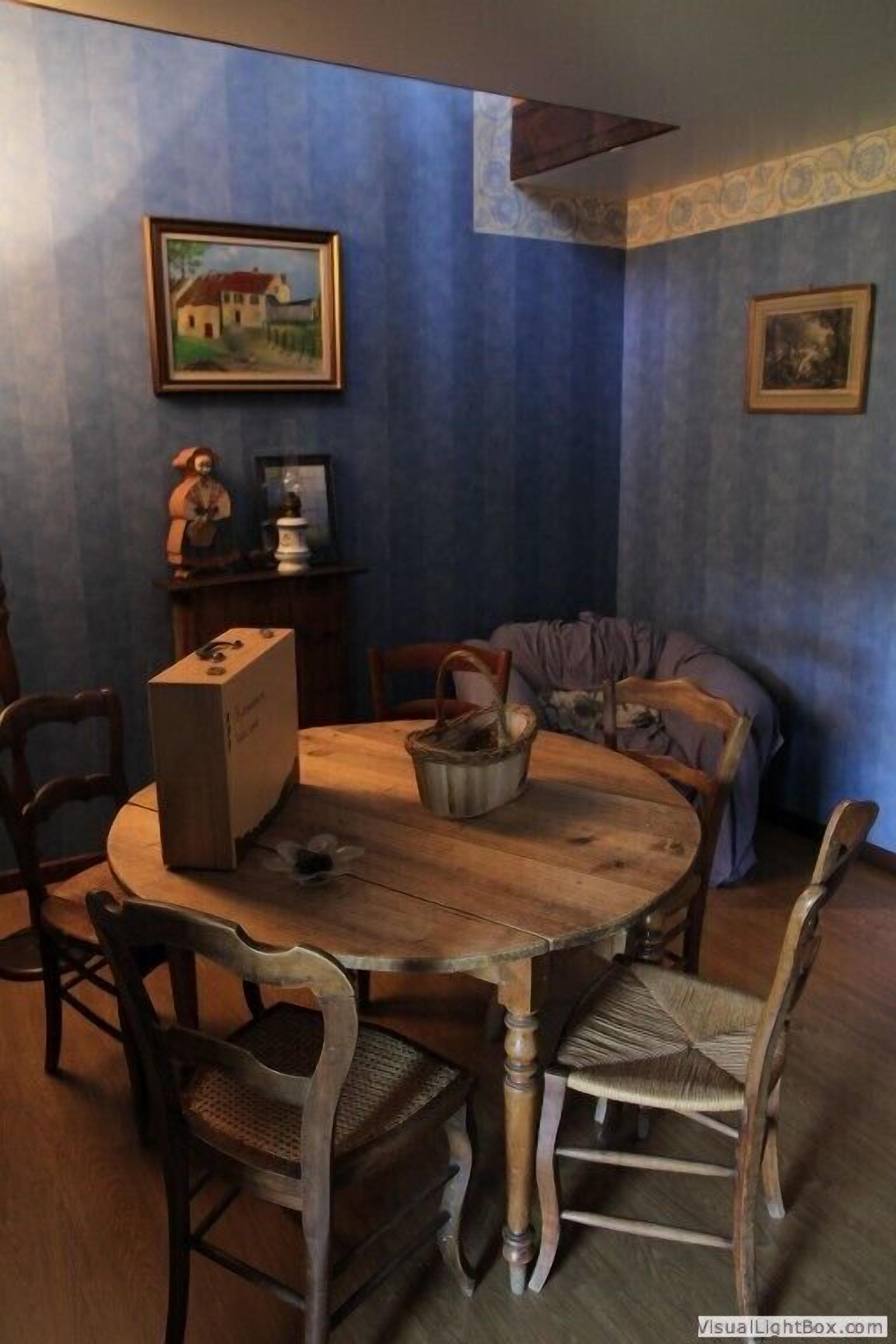 Un comedor con una mesa de madera, cuatro sillas, un florero y dos cuadros en las paredes.