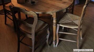 Un comedor con una mesa de madera, cuatro sillas, un florero y dos cuadros en las paredes.
