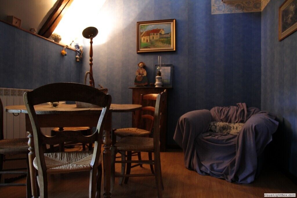 Una habitación con una mesa de comedor de madera, dos sillas, una mesita auxiliar con una lámpara, un cuadro en la pared y un sofá cubierto.