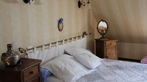 A bedroom with a sloped ceiling, a bed with white linens, a wooden nightstand with a lamp, and a dresser with a mirror.