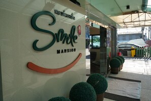 A hotel entrance with a sign reading "Smile Mansion" and potted plants in front. - Smile Mansion (Nakhon Si Thammarat)