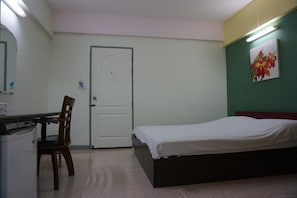 Une chambre à coucher avec un lit, un bureau et une chaise, une porte et un mur orné d’un tableau.
