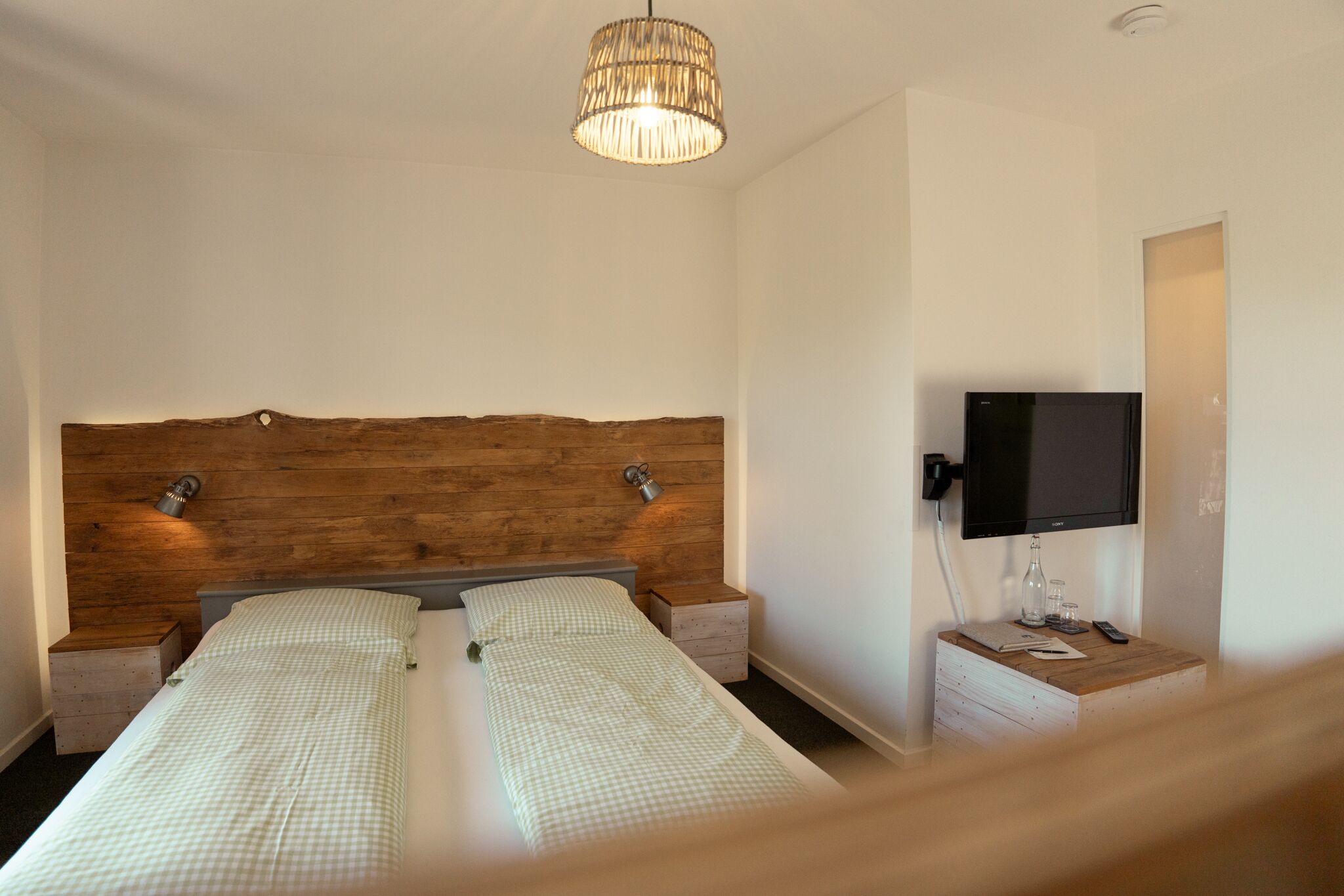 A bedroom with a wooden headboard, a television, bedside tables, and a hanging light fixture.