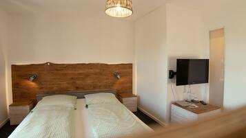 A bedroom with a wooden headboard, a television, bedside tables, and a hanging light fixture.