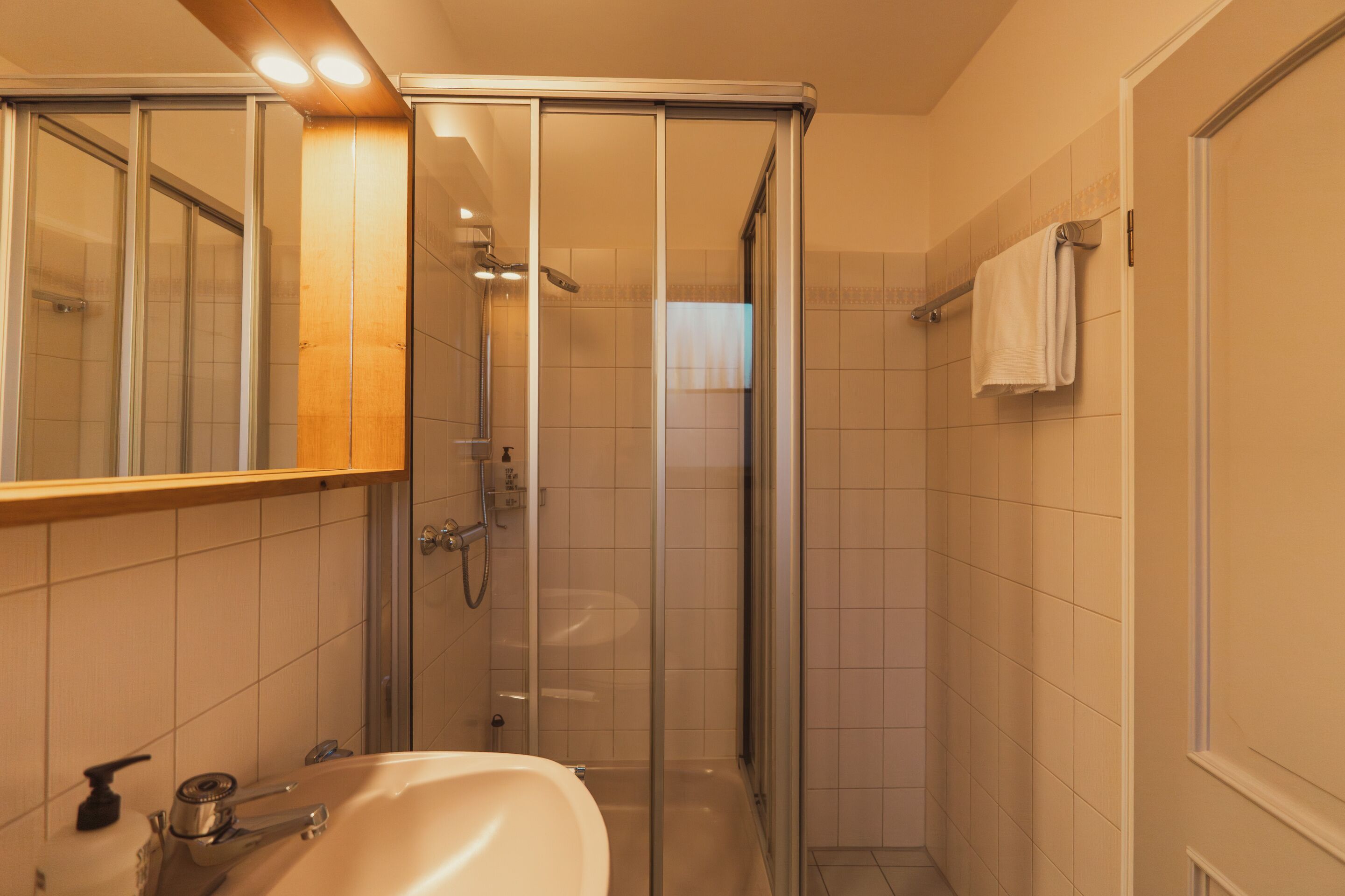 A bathroom with a glass shower enclosure, a sink with a mirror, and a towel rack.