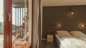 Un dormitorio con cama, mesitas de noche, una ventana con cortinas y vistas al exterior.
