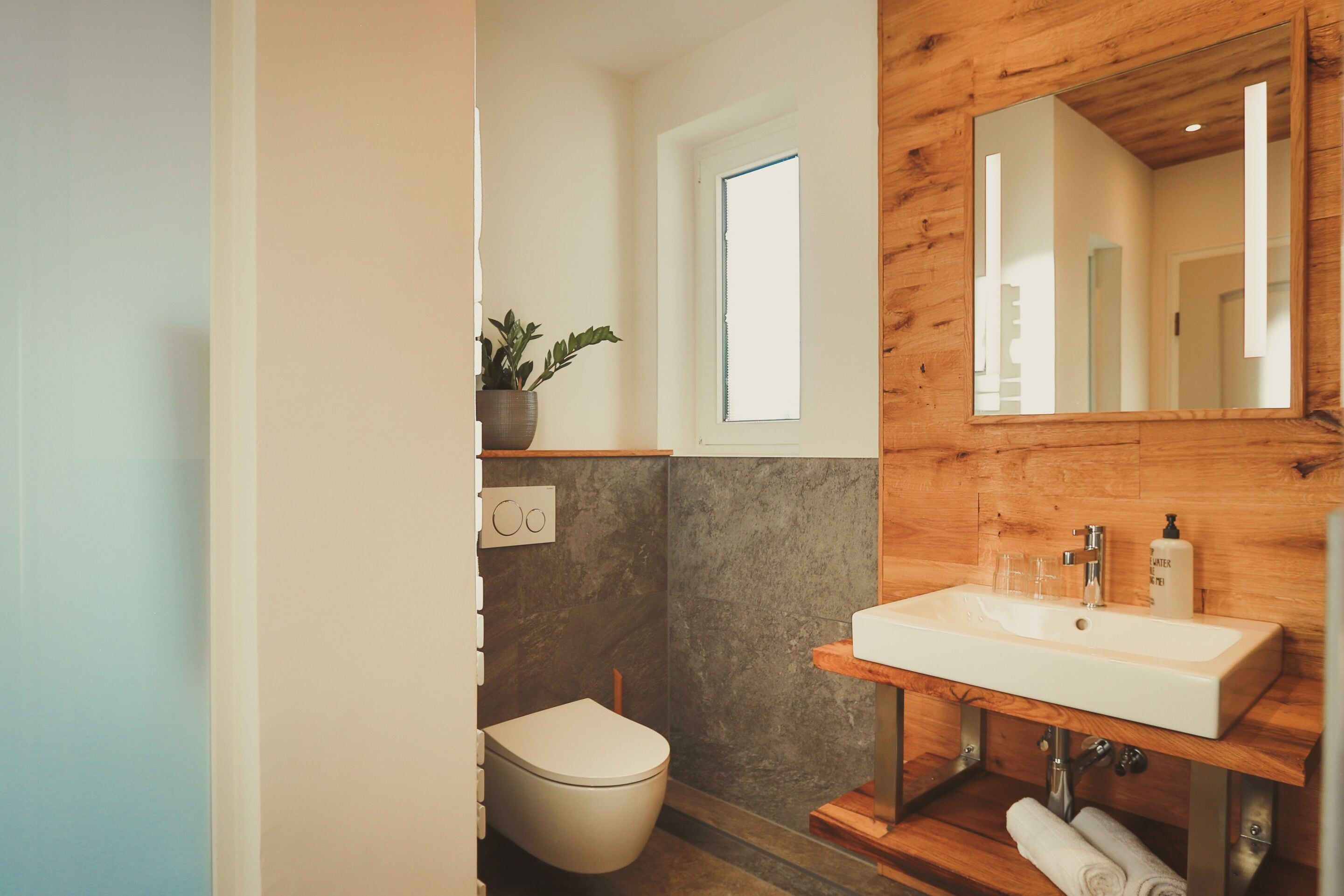 Ein modernes Badezimmer mit einem Holzkosmetikschrank, einem weißen Waschbecken und einer Toilette.