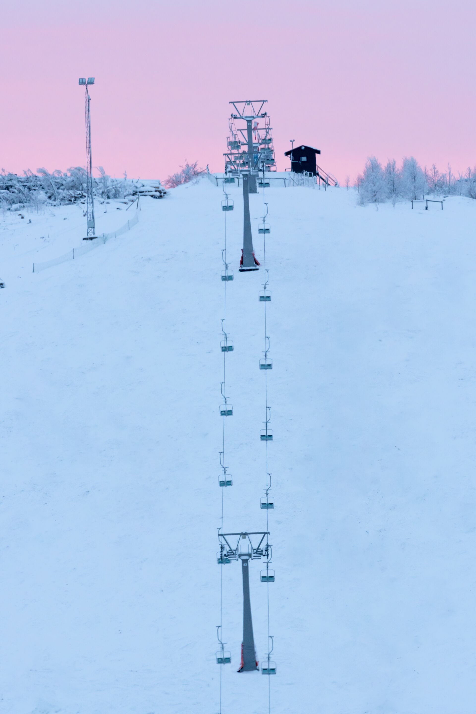 A ski lift on a snowy slope with a chairlift and a small cabin in the distance.