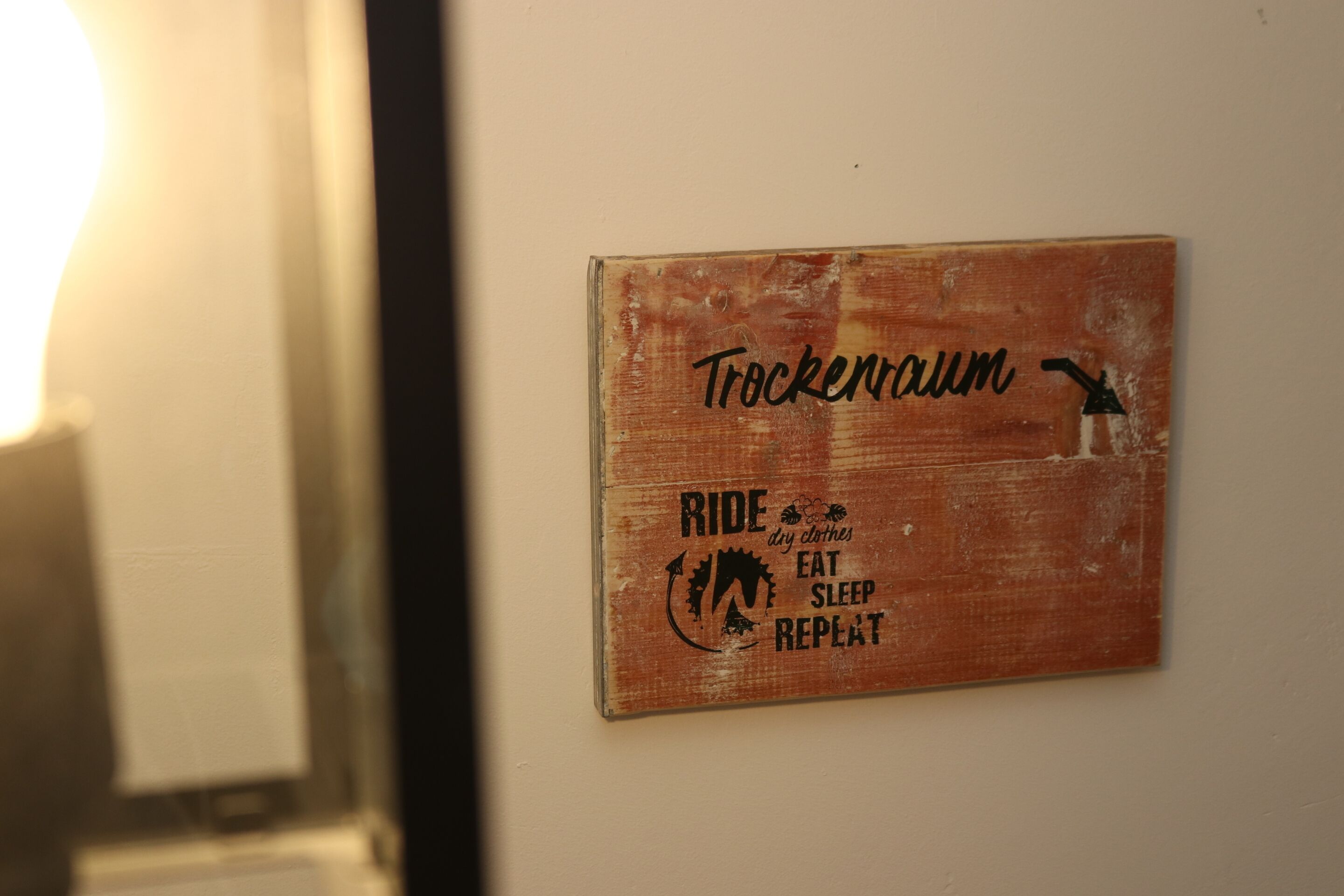 A wooden sign with the words "Trockennraum" and "Ride dry clothes eat sleep repeat" on a wall.