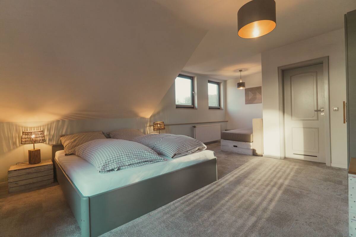A bedroom with a bed, two bedside tables, a lamp, a radiator, and a door.