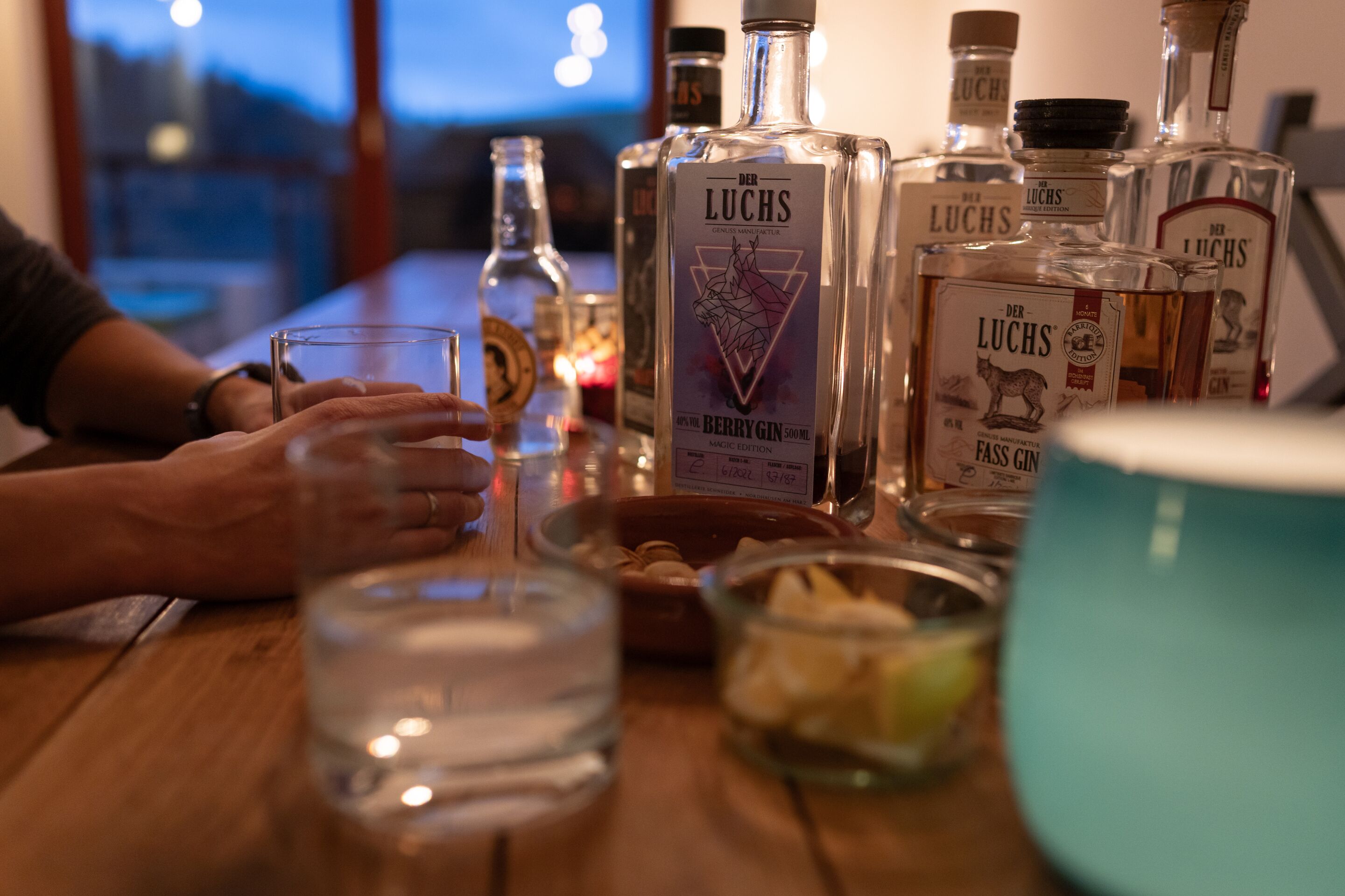 A bar setting with various bottles of Der Luchs gin, glasses, and a bowl of snacks.