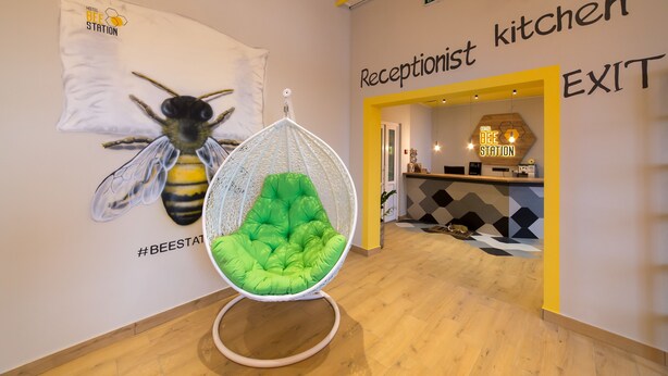 A reception area with a sign for the receptionist and kitchen, a hanging chair, and a wall decoration of a bee. - Hotel Bee Station - Hostel (Kyiv)