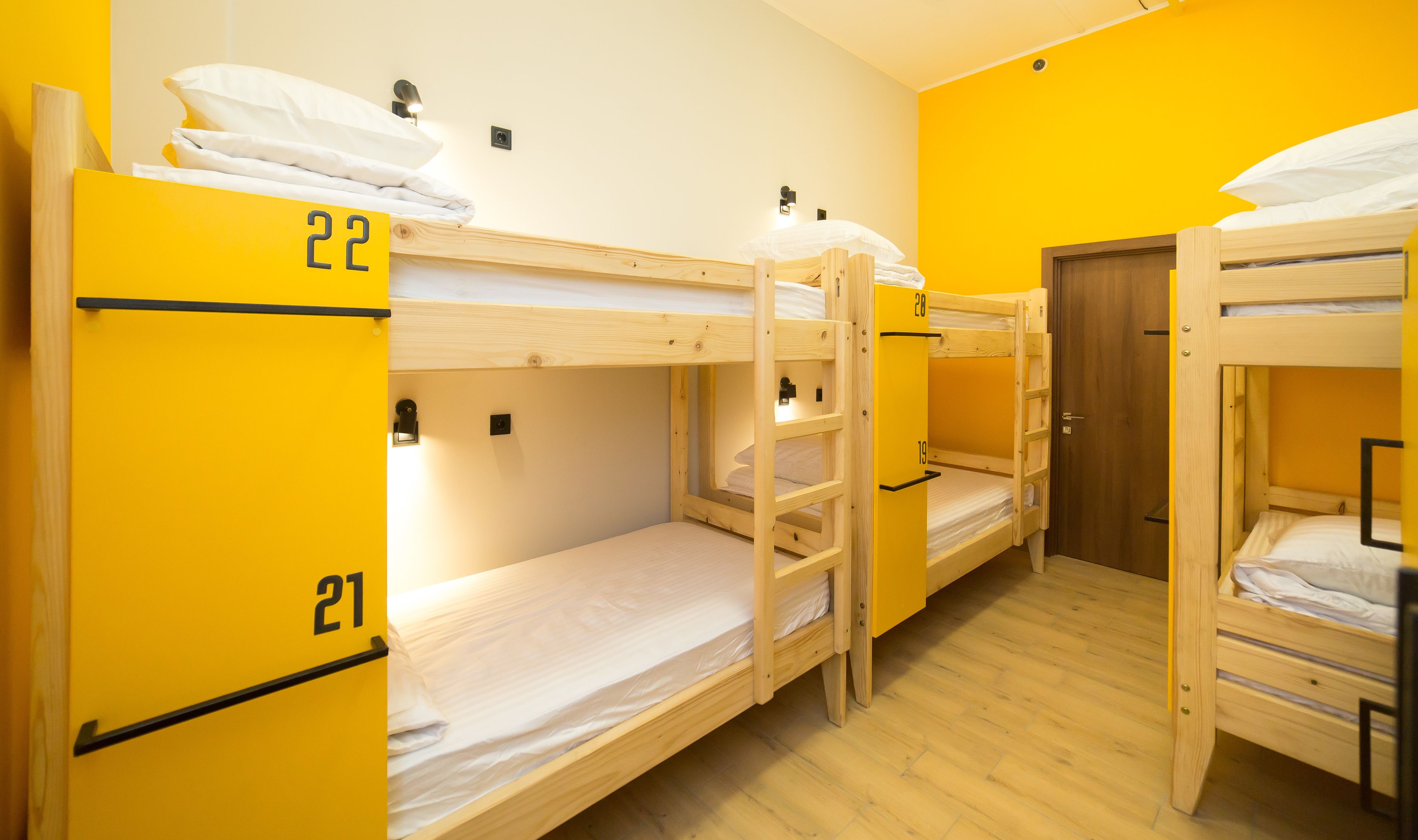 Habitación tipo dormitorio con literas numeradas 21, 22 y 28, suelo de madera y una puerta.
