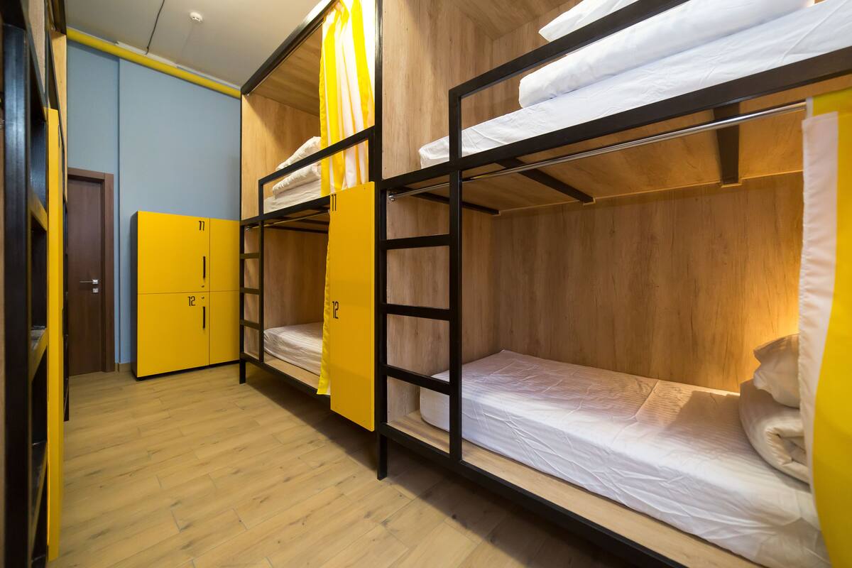 Asuntolan huone, jossa on kerrossängyt, keltainen vaatekaappi ja puulattia.
