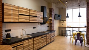 A modern kitchen with wooden cabinetry, a black countertop, and a brick wall. - Hotel Bee Station - Hostel (Kyiv)
