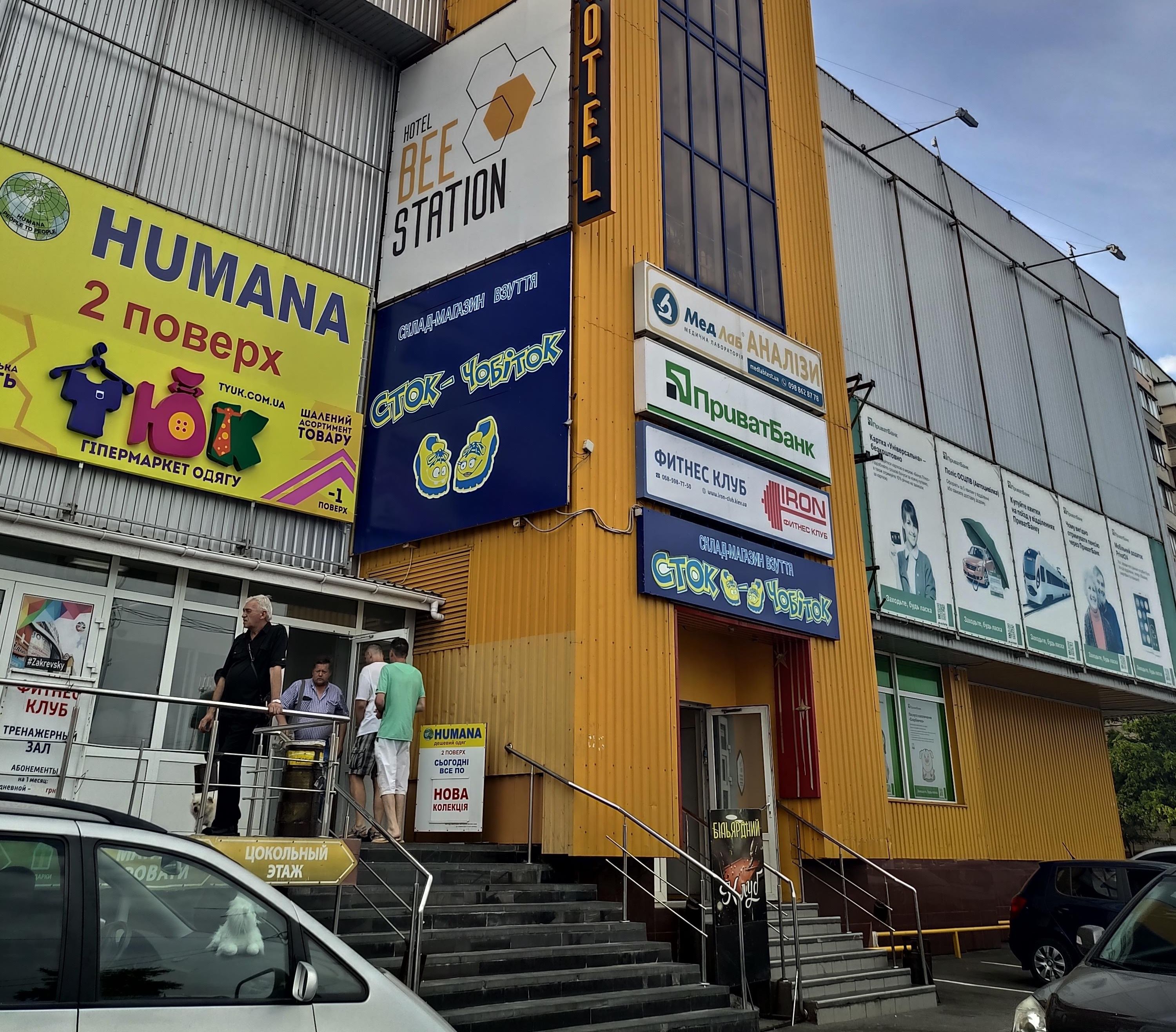 A building with multiple signs advertising various businesses, including a hotel, a supermarket, and a fitness club.