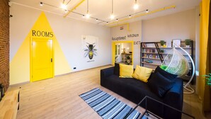 A modern interior with a yellow door labeled "ROOMS," a black sofa with yellow and green cushions, a hanging chair, and a bookshelf with books and plants. - Hotel Bee Station - Hostel (Kyiv)