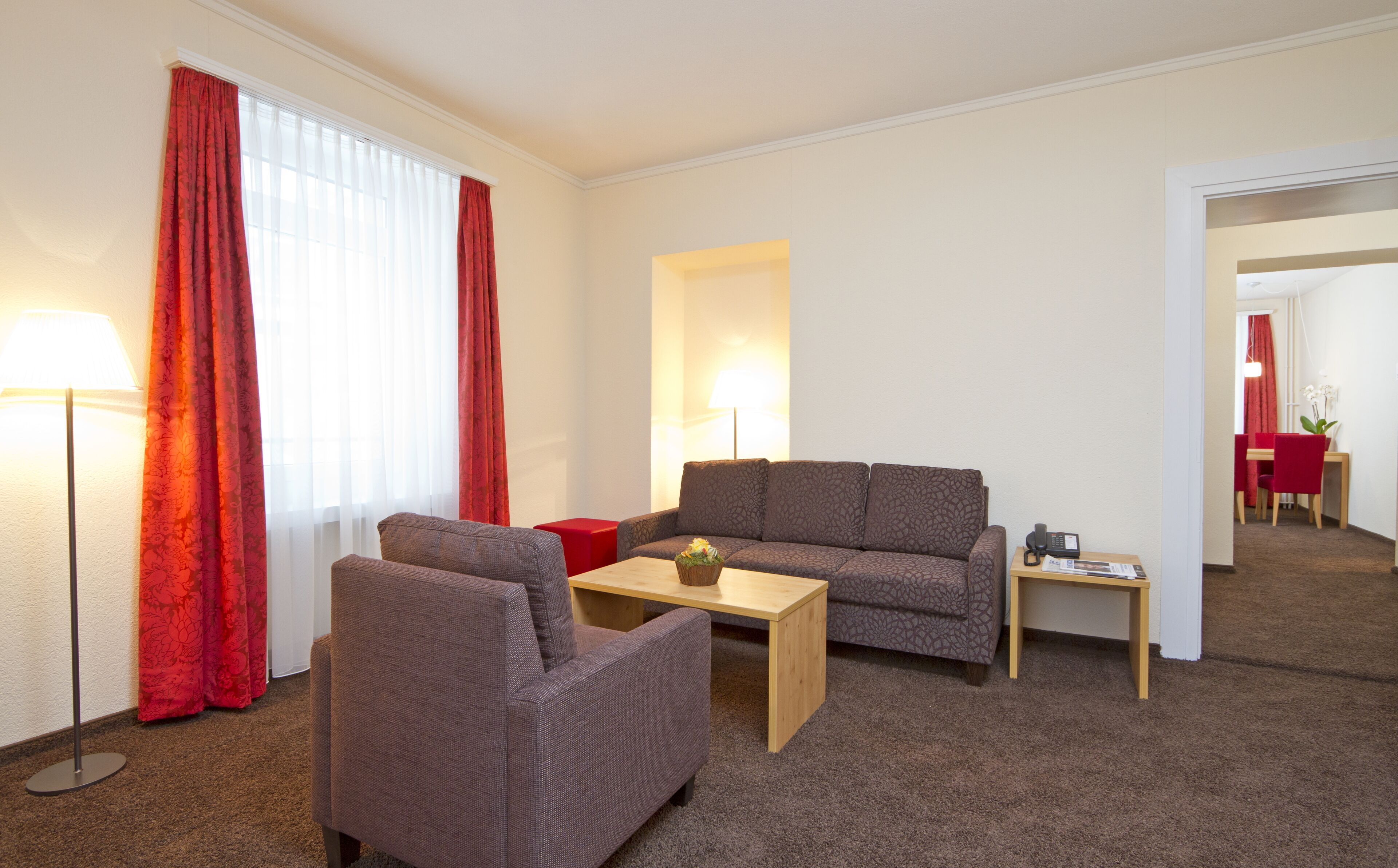 Een moderne woonkamer met een bank, fauteuil en salontafel. Er staat een lamp, een telefoon en een kleine tafel met een plantje.