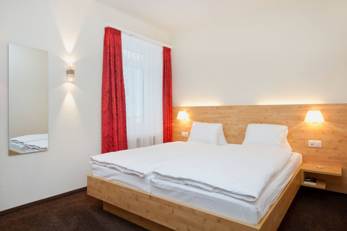 Una cama bien tendida con sábanas blancas, un cabecero de madera y dos lámparas de noche.