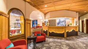 A lobby with a reception desk, red upholstered seating, a patterned carpet, and a large arched window. - Central Apartments Davos (Davos)