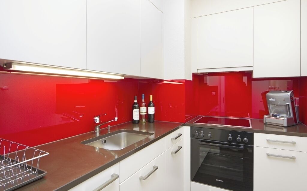 Una cucina moderna con mobili bianchi, un forno Bosch, un lavello e uno schienale rosso.